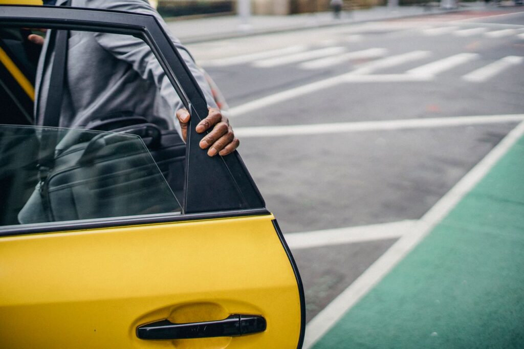 Crop anonymous African American male in elegant coat touching door of bright yellow automobile on asphalt road