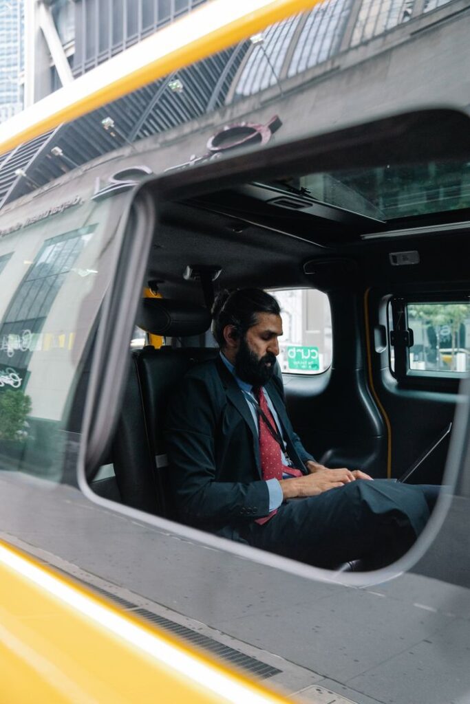A focused businessman working on a laptop inside a taxi, showcasing a modern work lifestyle.